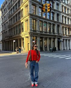 a woman standing in the middle of an intersection with traffic lights and buildings behind her