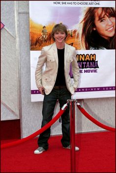 a man standing in front of a movie poster on a red carpeted area next to a barrier