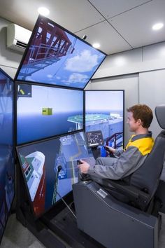 a man sitting in front of a computer monitor with multiple screens on the wall behind him