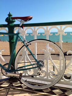 a bicycle parked on the side of a white fence next to water and beach in the background