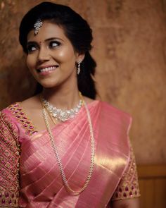 a woman in a pink sari with pearls on her head and necklace, smiling at the camera