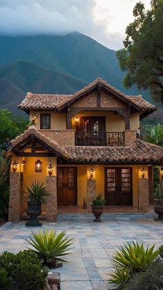 a house that is sitting in the middle of some plants and trees with mountains in the background