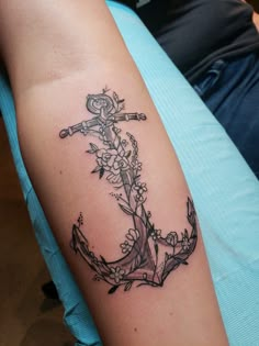 a black and white anchor with flowers on it's arm, sitting on a blue shirt