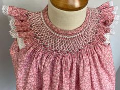 a pink dress with white lace on the neck and shoulders, sitting on a mannequin