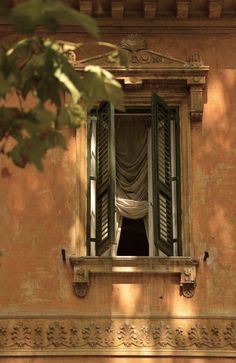 an open window on the side of a building with curtains hanging from it's windows