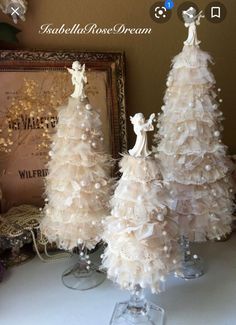 three white christmas trees sitting on top of a table next to a framed photo and other decorations