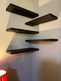 three wooden shelves mounted to the side of a wall next to a red table lamp