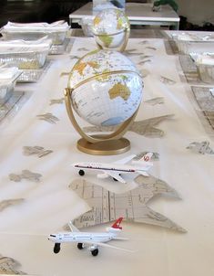 a table topped with lots of model airplanes and globes on top of paper plates