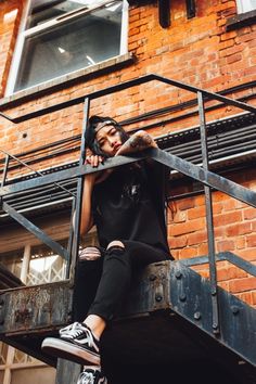 a woman sitting on the top of a metal hand rail next to a brick building