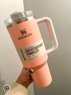 a person holding up a pink tumbler with the word stanley on it in front of a white wall