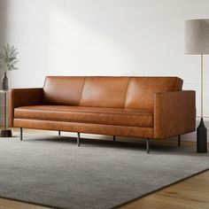 a brown leather couch sitting on top of a wooden floor next to a lamp and rug