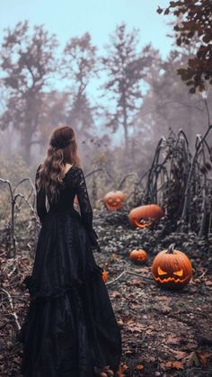 a woman in a long black dress is looking at pumpkins