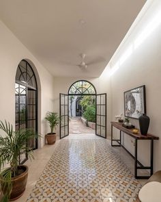 a hallway with an arched window and tiled flooring, potted plants on either side