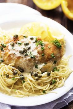 a white plate topped with pasta and meat next to lemon wedges on a wooden table