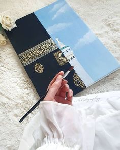 a person holding a pen in front of a book on a bed with flowers and a white rose