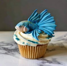 a cupcake with blue frosting and a fish decoration on it's side