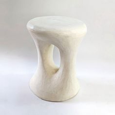 a small white ceramic stool with a hole in the middle on a plain surface,