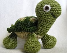 a crocheted green turtle sitting on top of a white table next to a stuffed animal