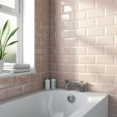 a white bath tub sitting under a window next to a green plant in a vase