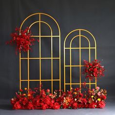 red flowers are growing out of the top of an iron trellis with arched windows