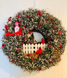 a wreath hanging on the side of a white door with red birds and pine cones