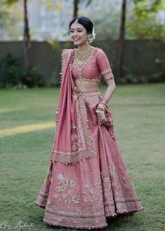 a woman in a pink lehenga standing on grass