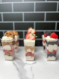 four desserts with strawberries, chocolate chip cookies and whipped cream on top are lined up in small cups