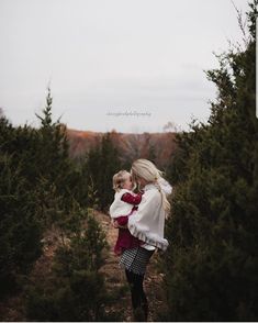 a woman holding a baby in her arms while walking through a forest filled with trees