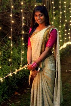 a woman in a white sari standing next to some string lights and greenery