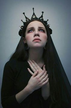 a woman with long hair wearing a crown on her head and holding her hands to her chest