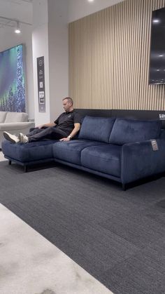 a man sitting on top of a blue couch in a living room next to a wall