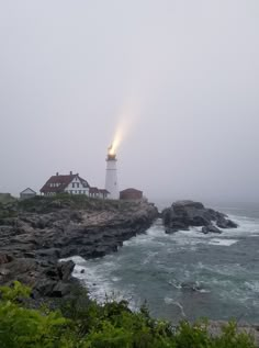 a light house sitting on top of a rocky cliff next to the ocean with fog