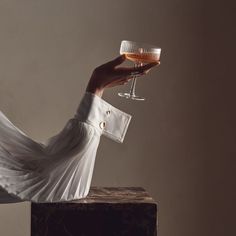 a woman holding a glass of wine on top of a wooden block in front of a wall