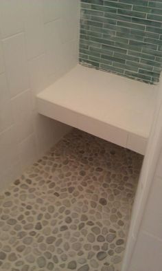 a white bench sitting in a bathroom next to a walk in shower stall with pebbles on the floor