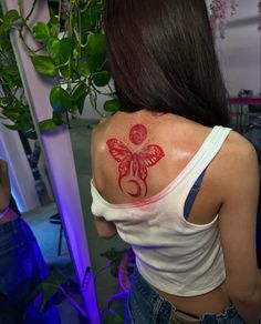 a woman with a butterfly tattoo on her upper back shoulder and arm, in front of a plant