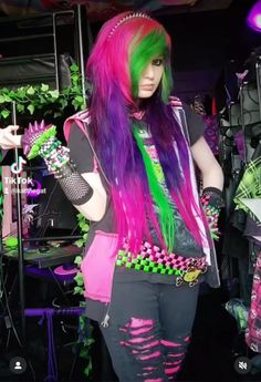 a woman with green and purple hair standing in front of a stage wearing punk clothing