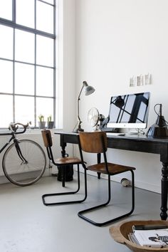 a desk with two chairs and a computer on top of it in front of a window