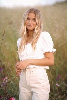 a woman standing in the middle of a field with wildflowers on her side