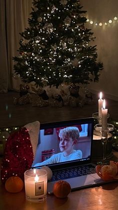 a laptop computer sitting on top of a wooden table next to candles and oranges