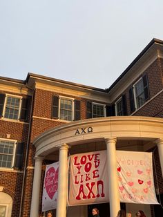 people are standing on the front porch of a large brick building with banners hanging from it's sides