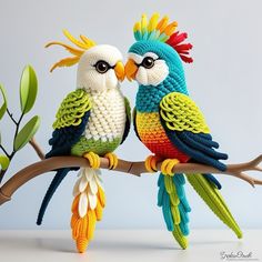 two crocheted parrots sitting on a branch with their beaks touching each other