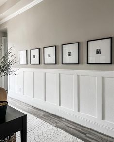 a living room with white paneling and pictures hanging on the wall, along with a vase filled with baby's breath flowers