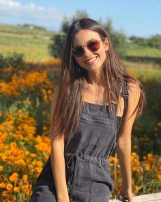 a young woman sitting on a wooden bench in front of yellow and orange wildflowers