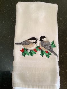 two birds sitting on top of a white towel with holly and berries embroidered on it