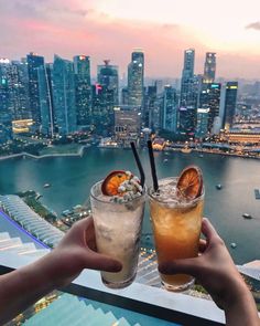 two people holding up drinks in front of a cityscape