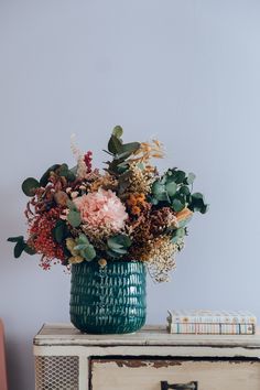 a vase filled with lots of flowers sitting on top of a wooden table next to a book