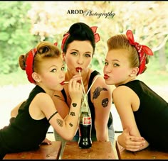 three beautiful young women sitting at a table with a bottle in their hands and one holding a straw up to her mouth