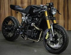 a black and gold motorcycle parked in front of a wooden wall on concrete flooring