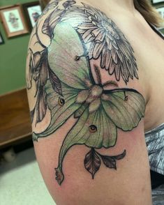 a woman's shoulder with a green flower and wings tattoo on her left arm