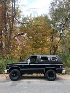 a black truck parked on the side of a road in front of trees with orange leaves